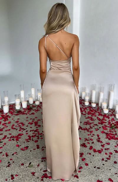 Back view of a champagne one-shoulder draped maxi dress, showing the thin strap and open back design.