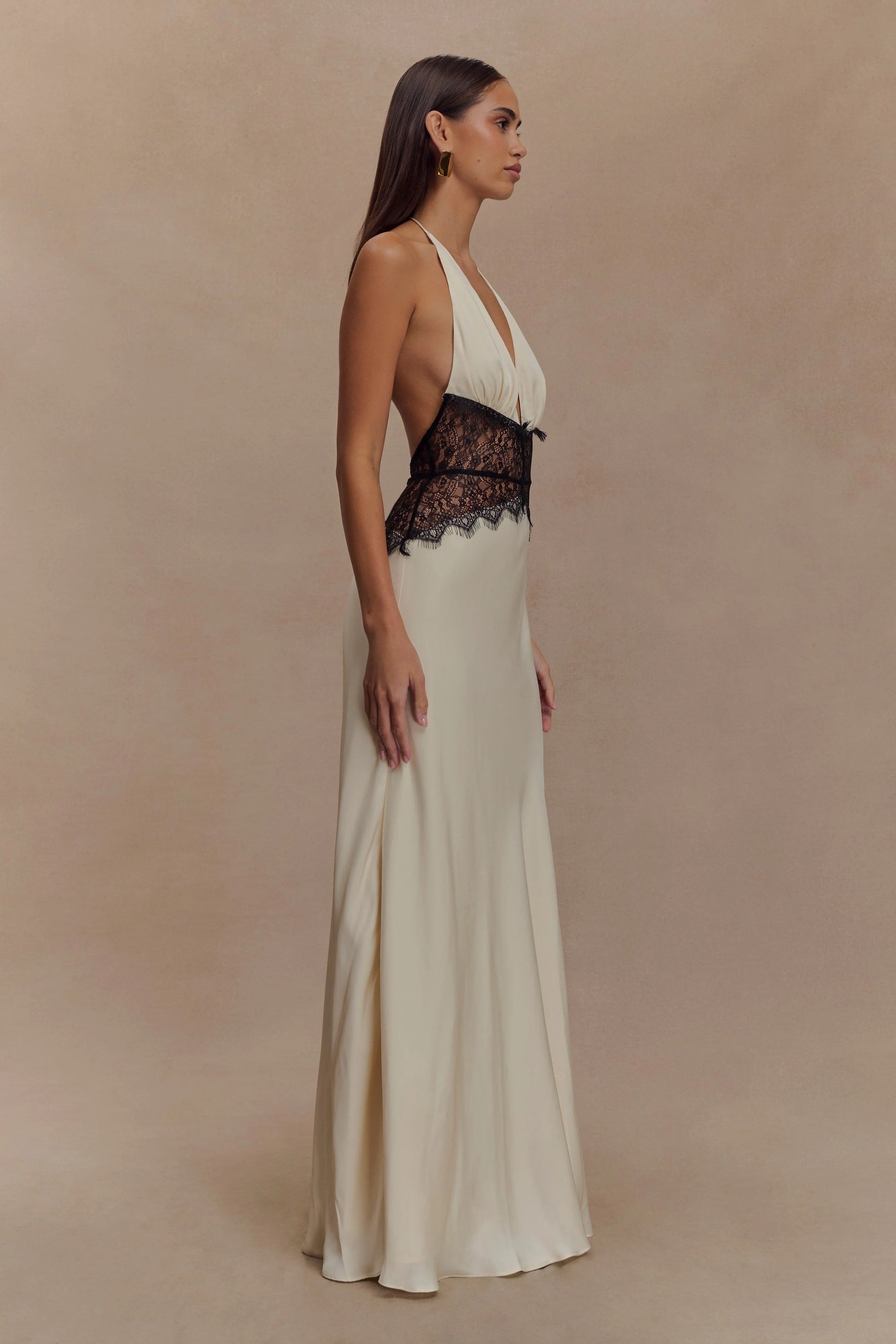 Side profile of a cream Skye Lace Maxi Dress with a deep V-neck and black lace bodice detail, flowing skirt.