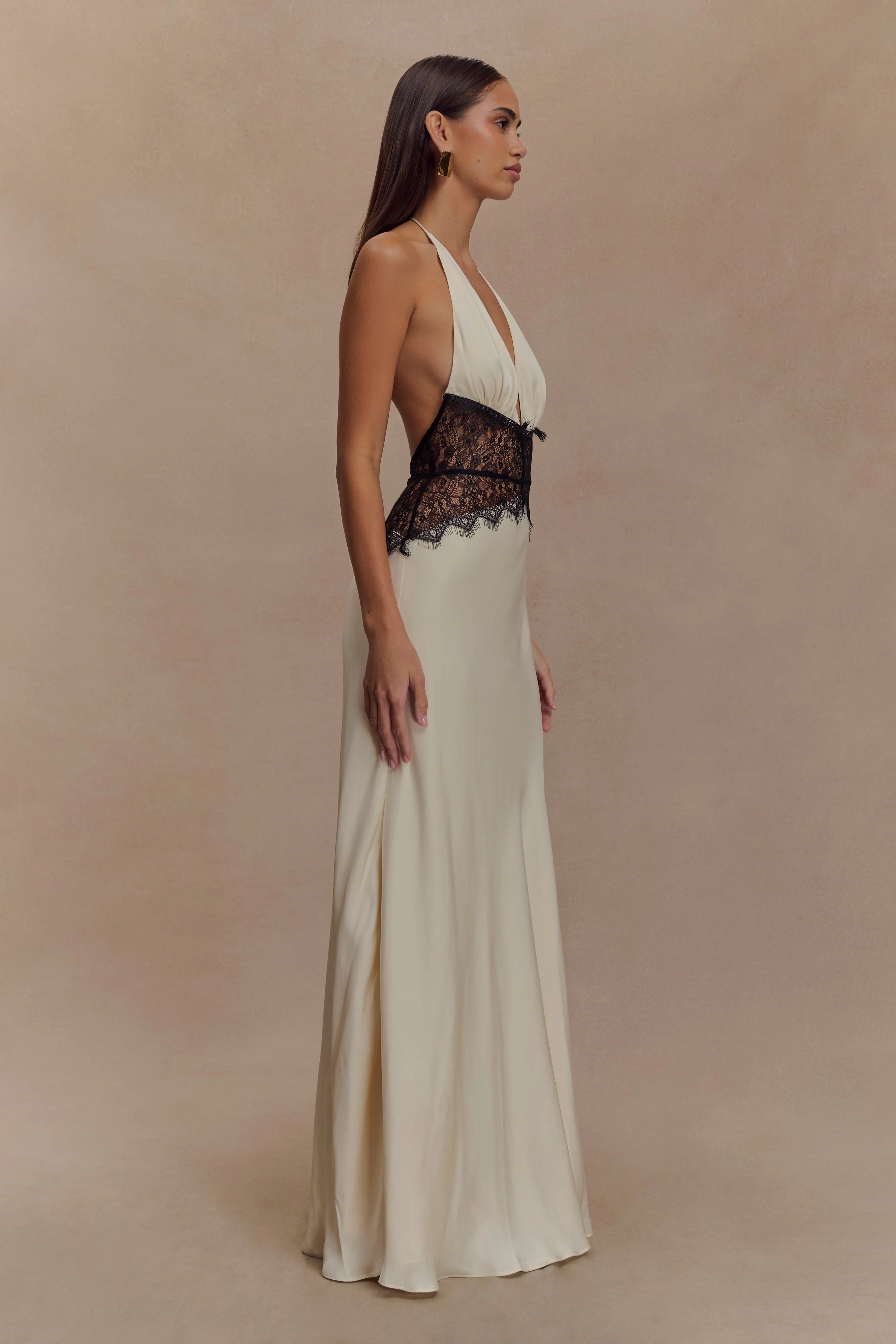 Side profile of a cream Skye Lace Maxi Dress with a deep V-neck and black lace bodice detail, flowing skirt.