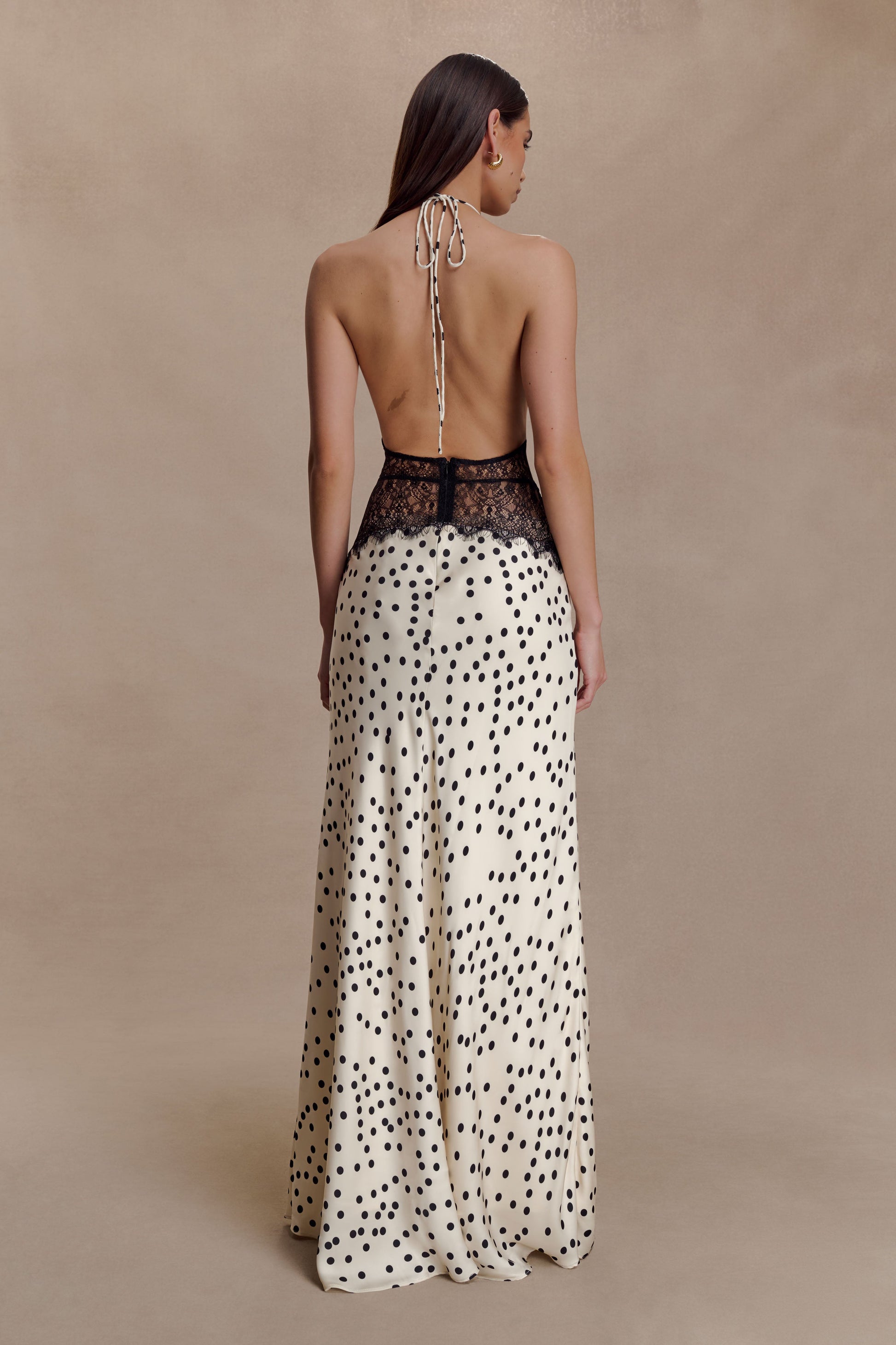 Back view of the cream Skye Lace Maxi Dress with black polka dots, revealing an open back and halter tie closure.