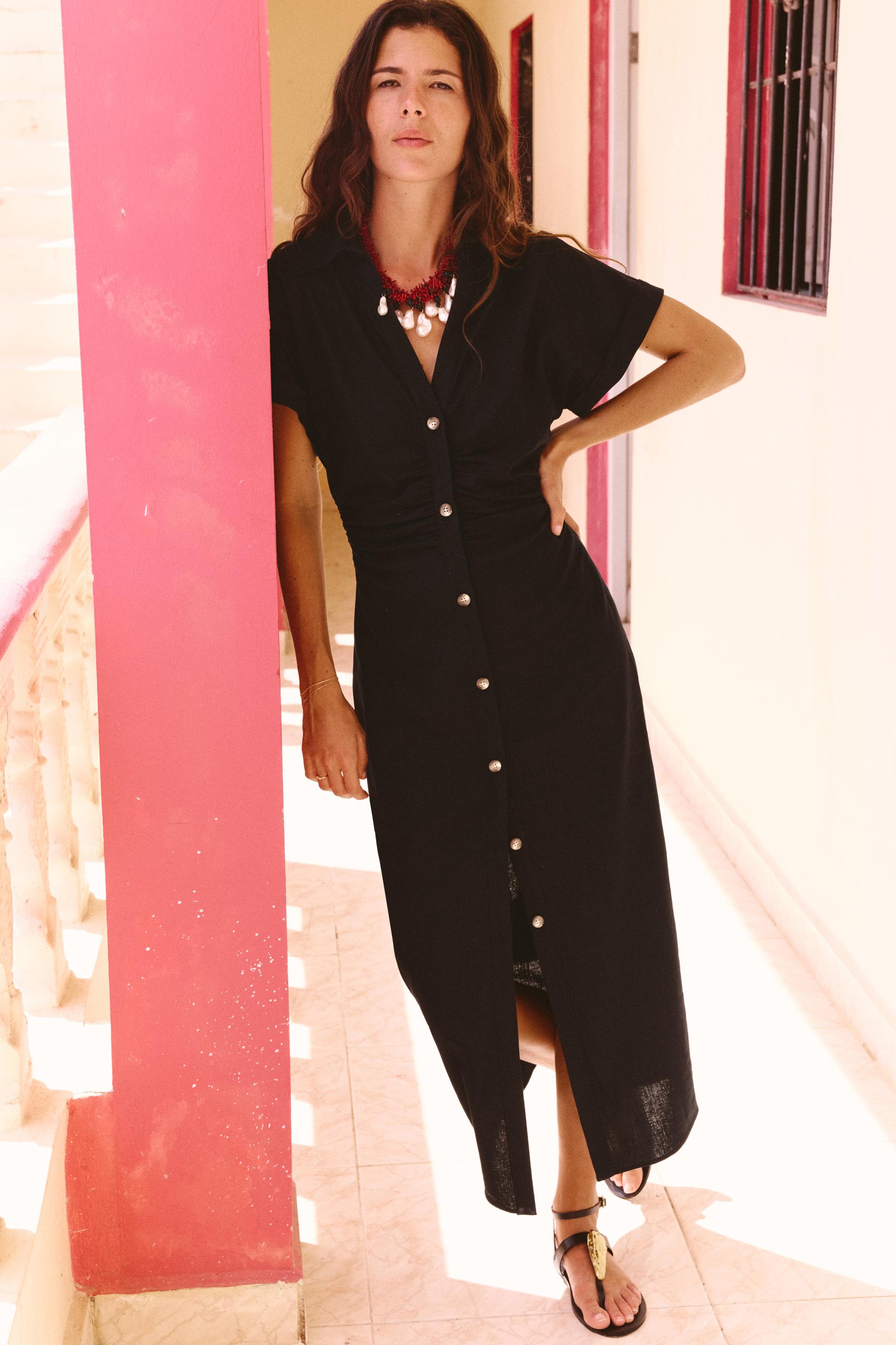 Black button-front midi dress with gold buttons, short sleeves, and a ruched waist, styled with a red and white statement necklace.