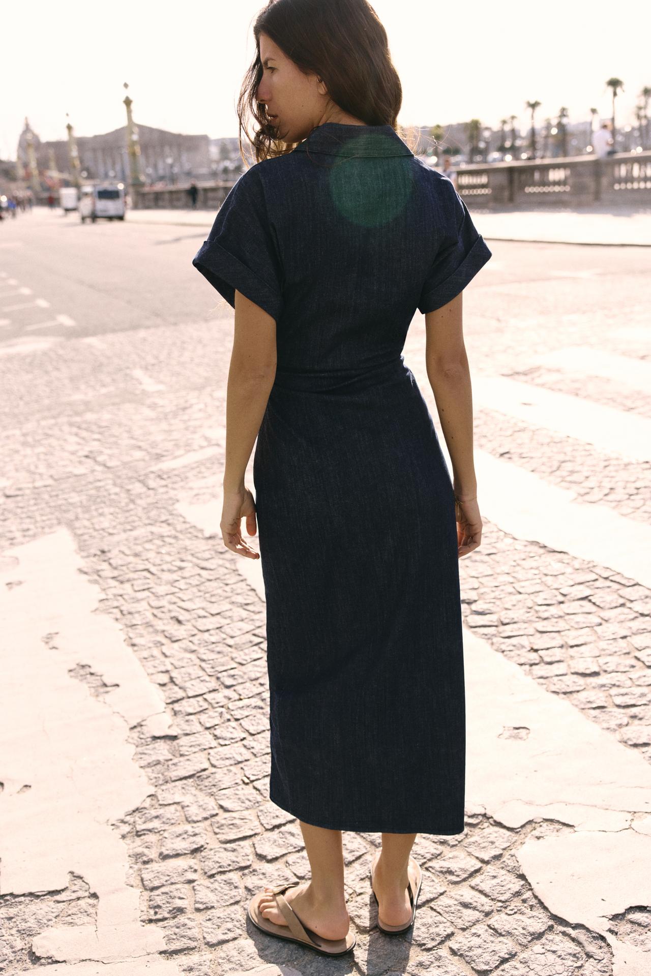 Back view of the dark wash denim Sofia button midi dress, showing the short sleeves and natural waistline, worn with flat sandals.