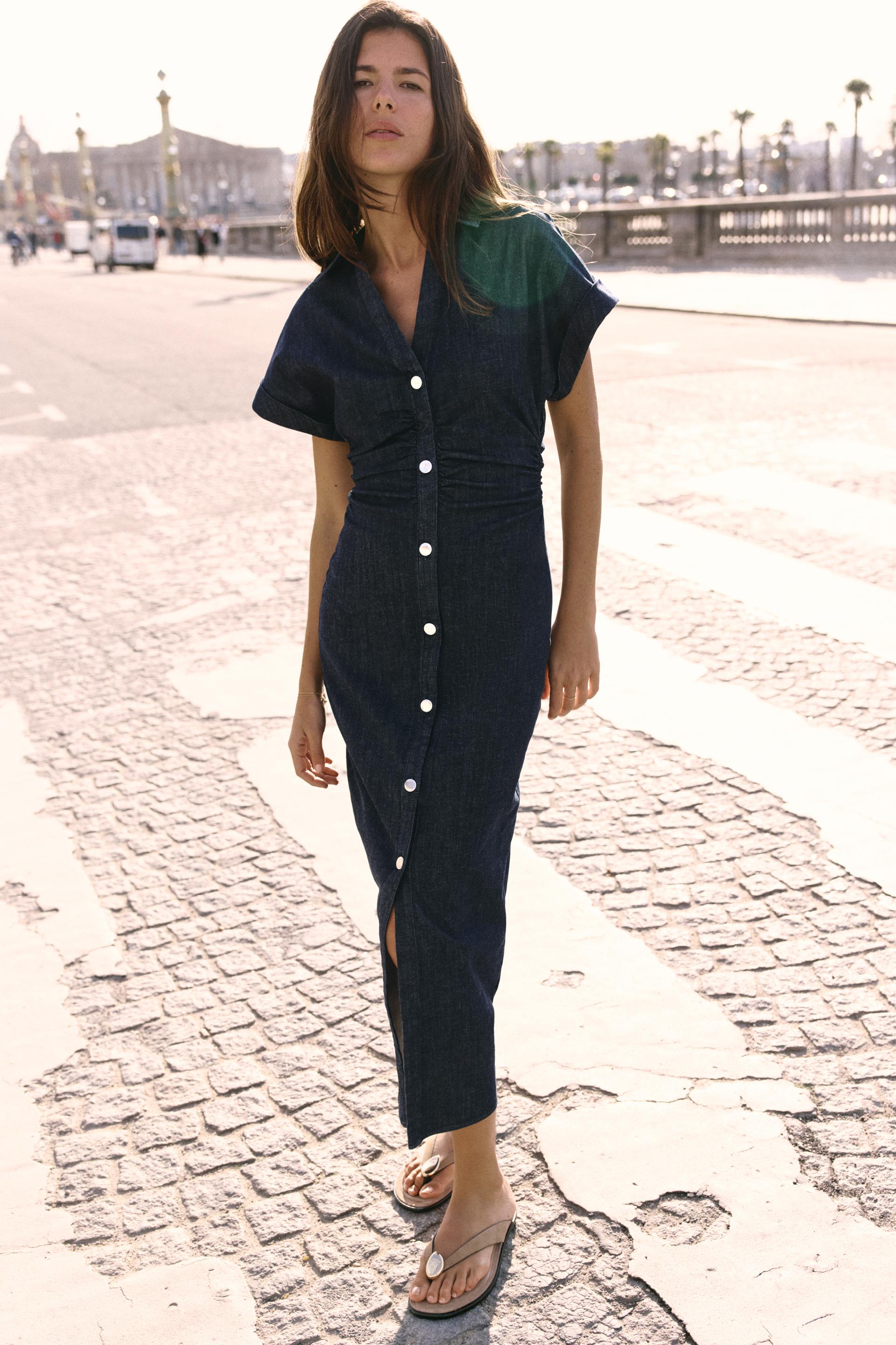 Full body shot of the dark wash denim Sofia button midi dress with a front slit, white buttons, and short sleeves, worn with sandals.