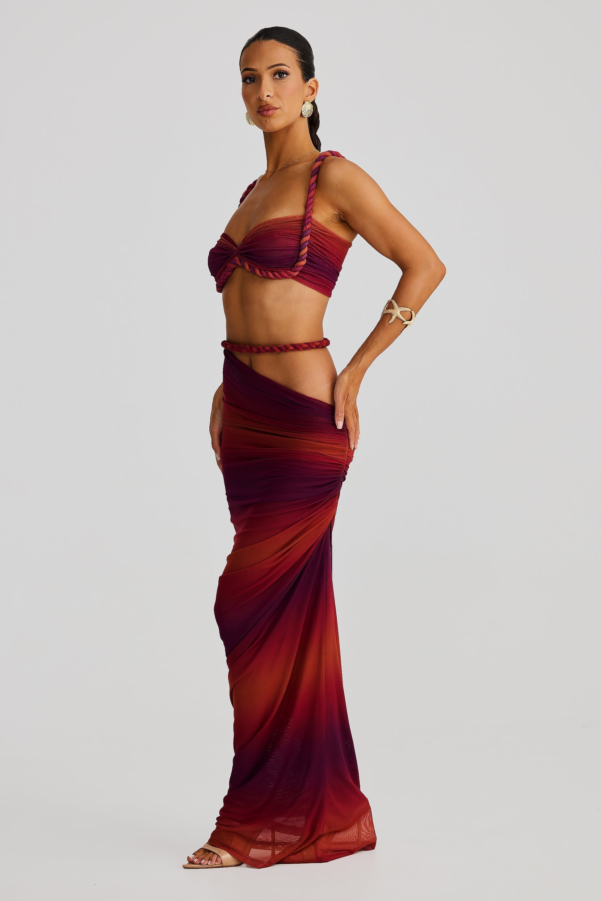 Side view of a red ombre Sophie Braided Maxi Set, featuring a braided top and a draped maxi skirt with a high slit.
