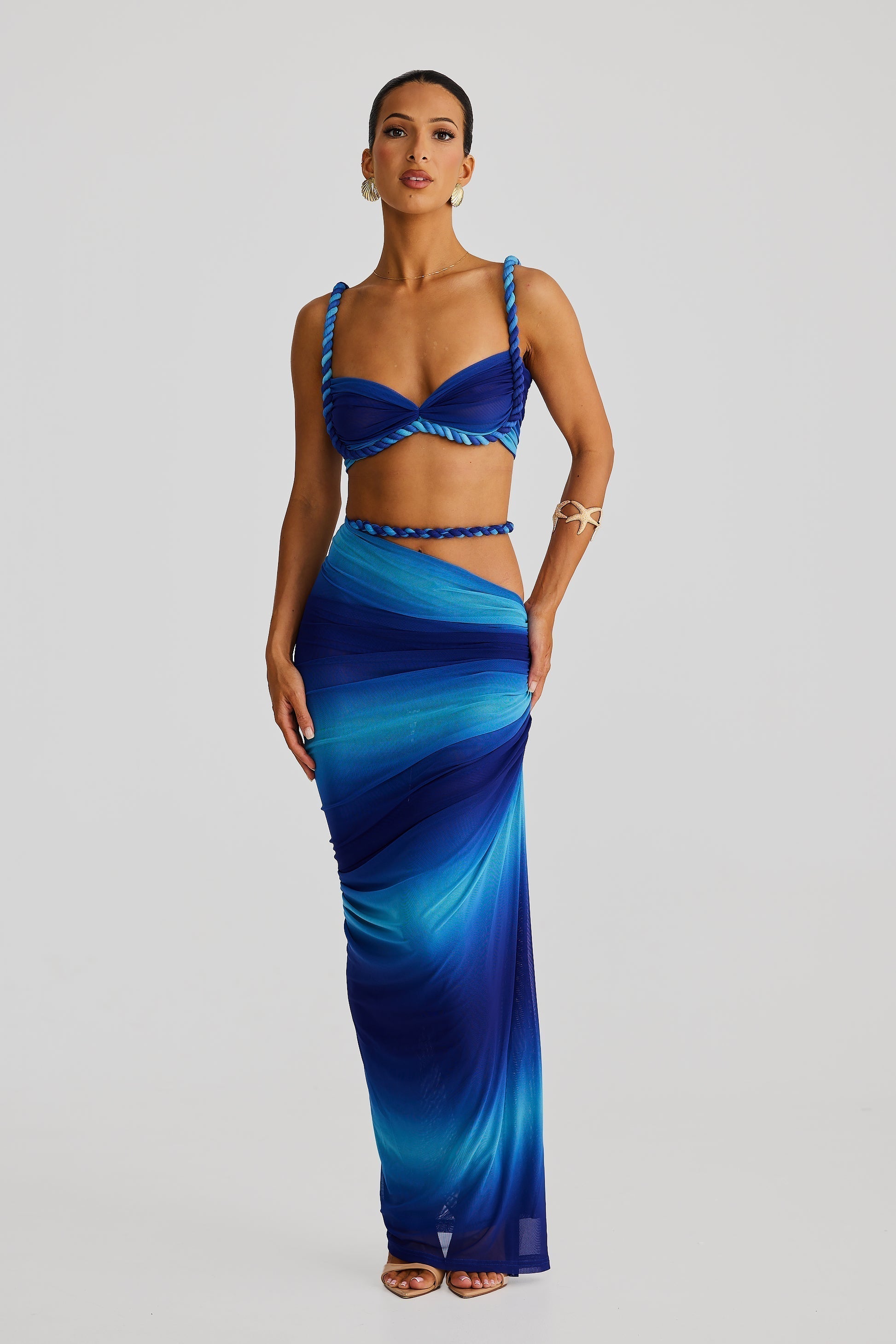 Full-length view of a woman in a blue ombre braided maxi set, featuring a bandeau top and a flowing, draped maxi skirt.