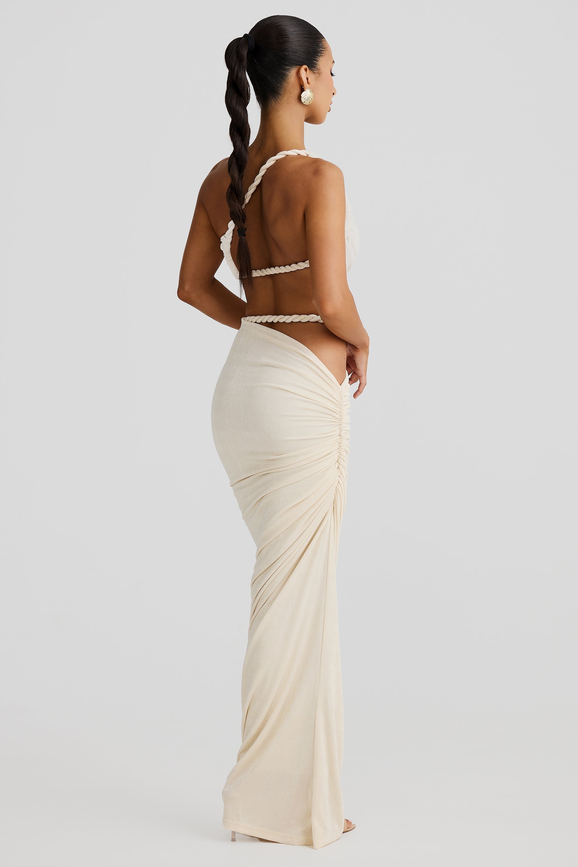 Rear view of a woman in a cream braided maxi set, showing the back of the bandeau top and the ruched detailing on the maxi skirt.