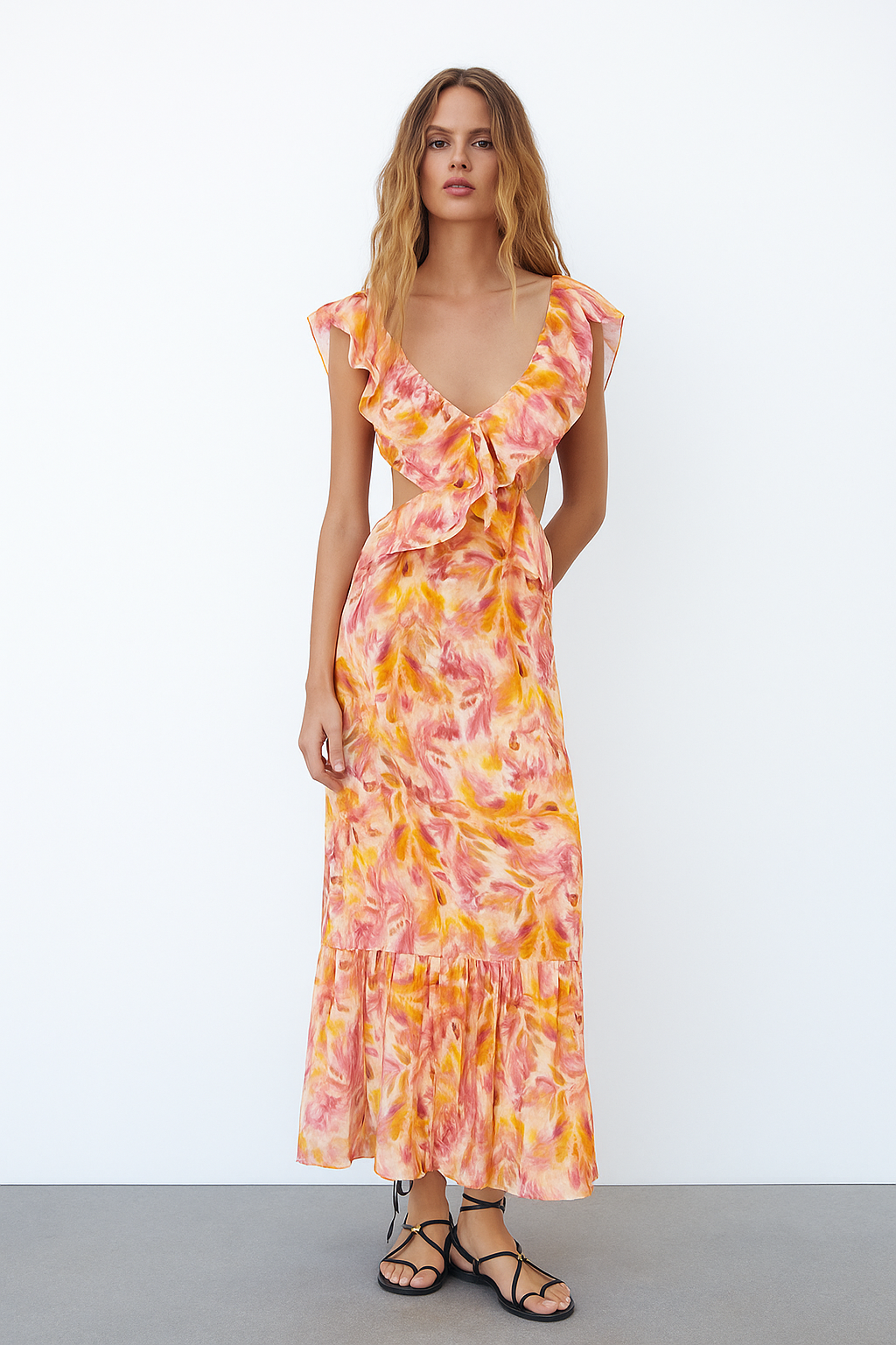 Full-length view of a woman wearing a Sunniva cutout maxi dress in a colorful floral print, paired with black sandals.