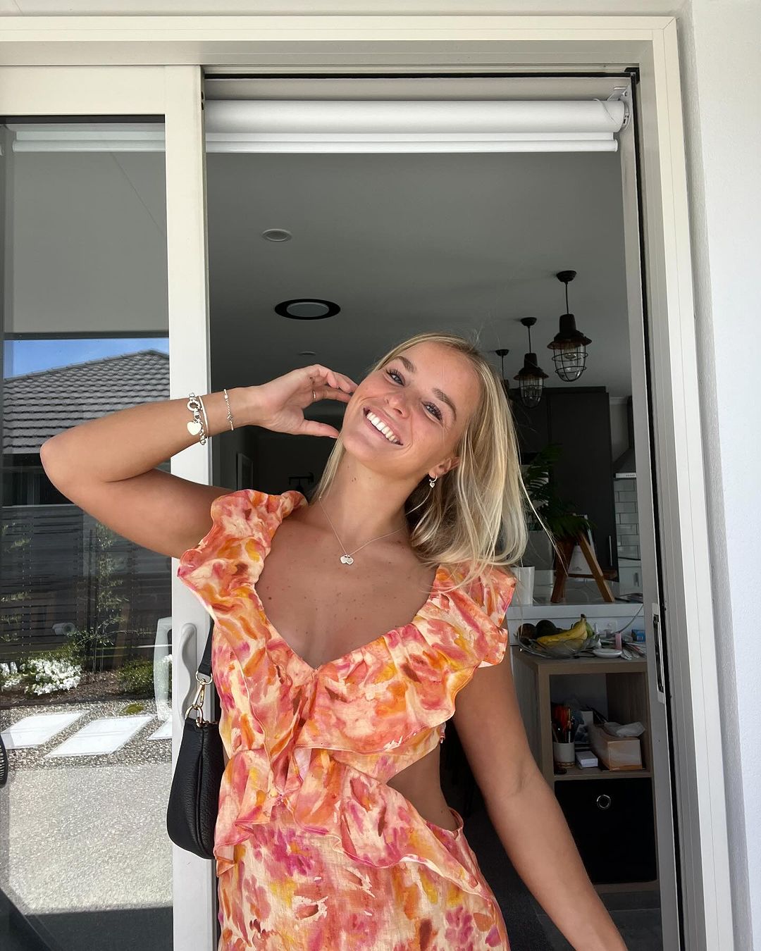 Happy woman posing in a vibrant orange and pink floral Sunniva cutout maxi dress with a deep V-neck and ruffled cap sleeves.