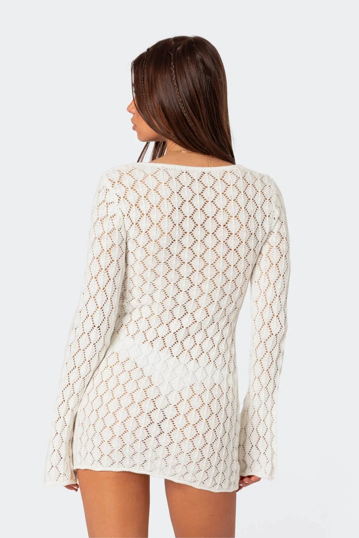 Back view of a woman in a white crochet mini dress, showing the full length of the long sleeves and knit pattern.