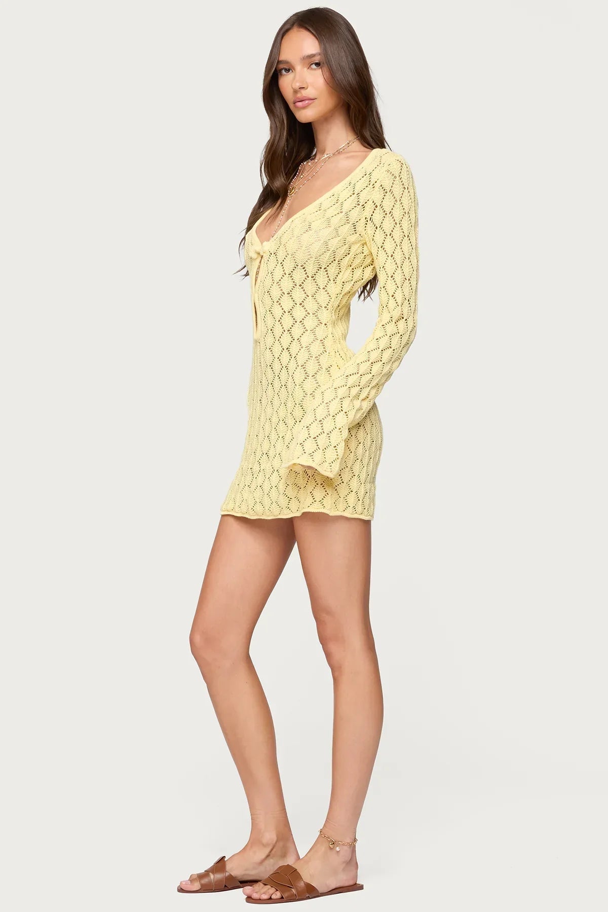 Side profile of a woman wearing a light yellow crochet keyhole mini dress, showcasing the long sleeves.