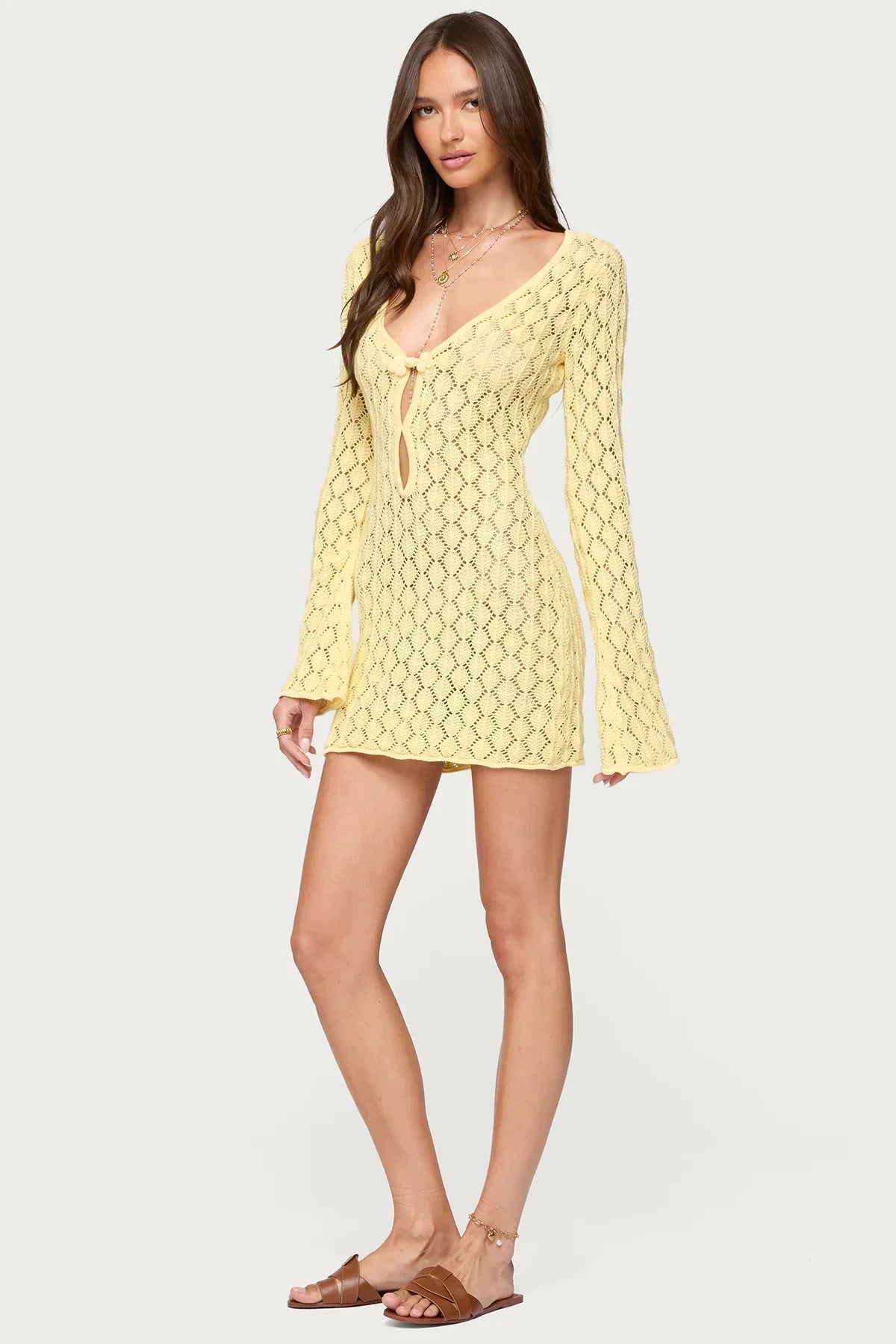Front slightly angled view of a woman in a yellow crochet keyhole mini dress with bell sleeves.