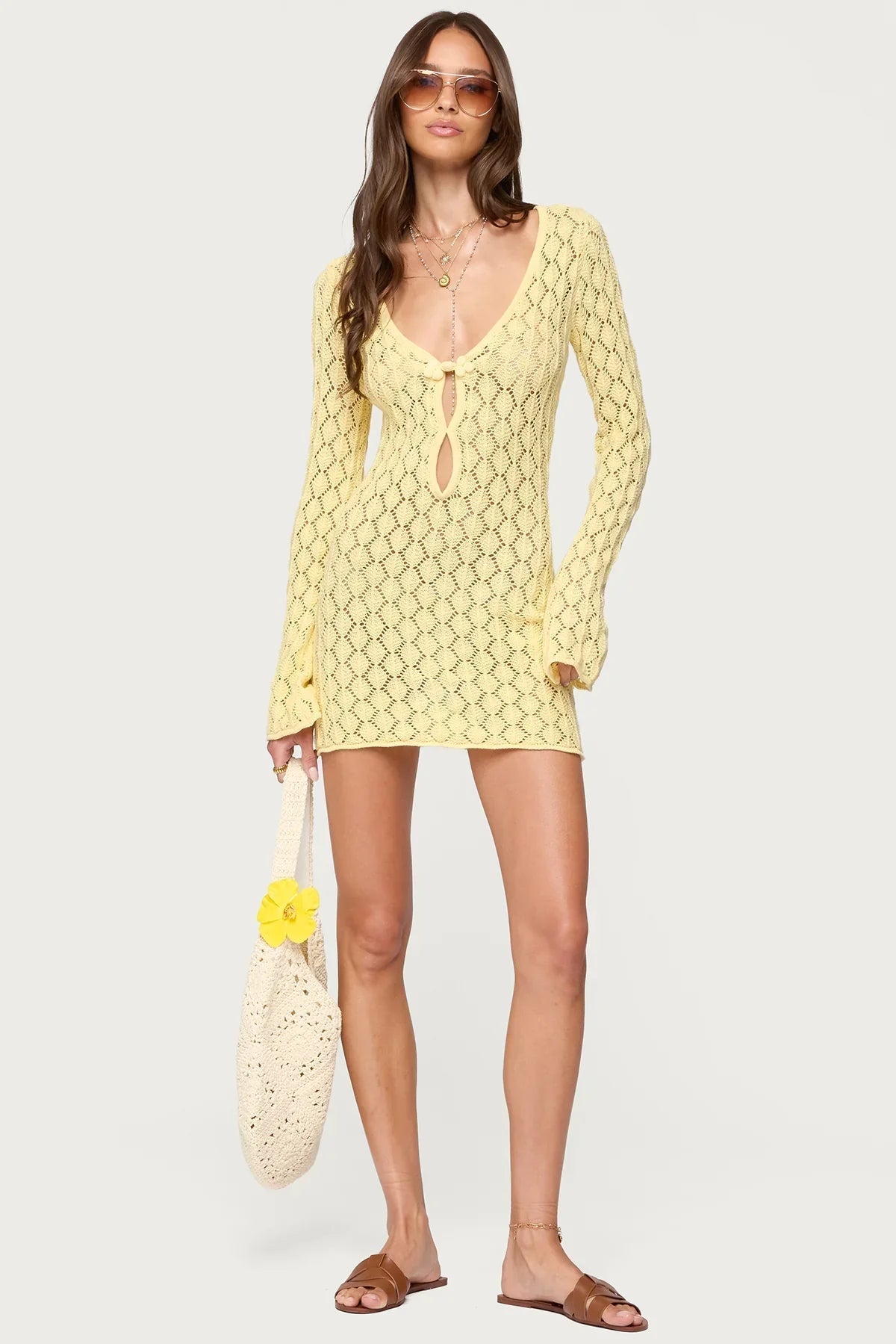 Full shot of a woman in a yellow crochet mini dress with a keyhole detail and long sleeves, wearing sunglasses.