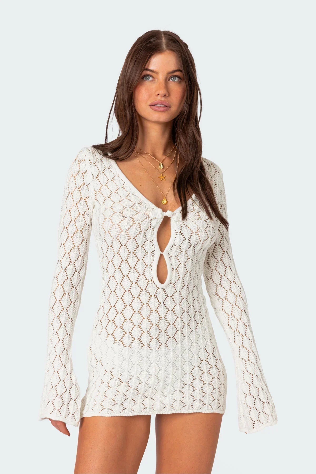 Close-up of a woman's face and upper body in a white crochet keyhole mini dress, showing necklace details.