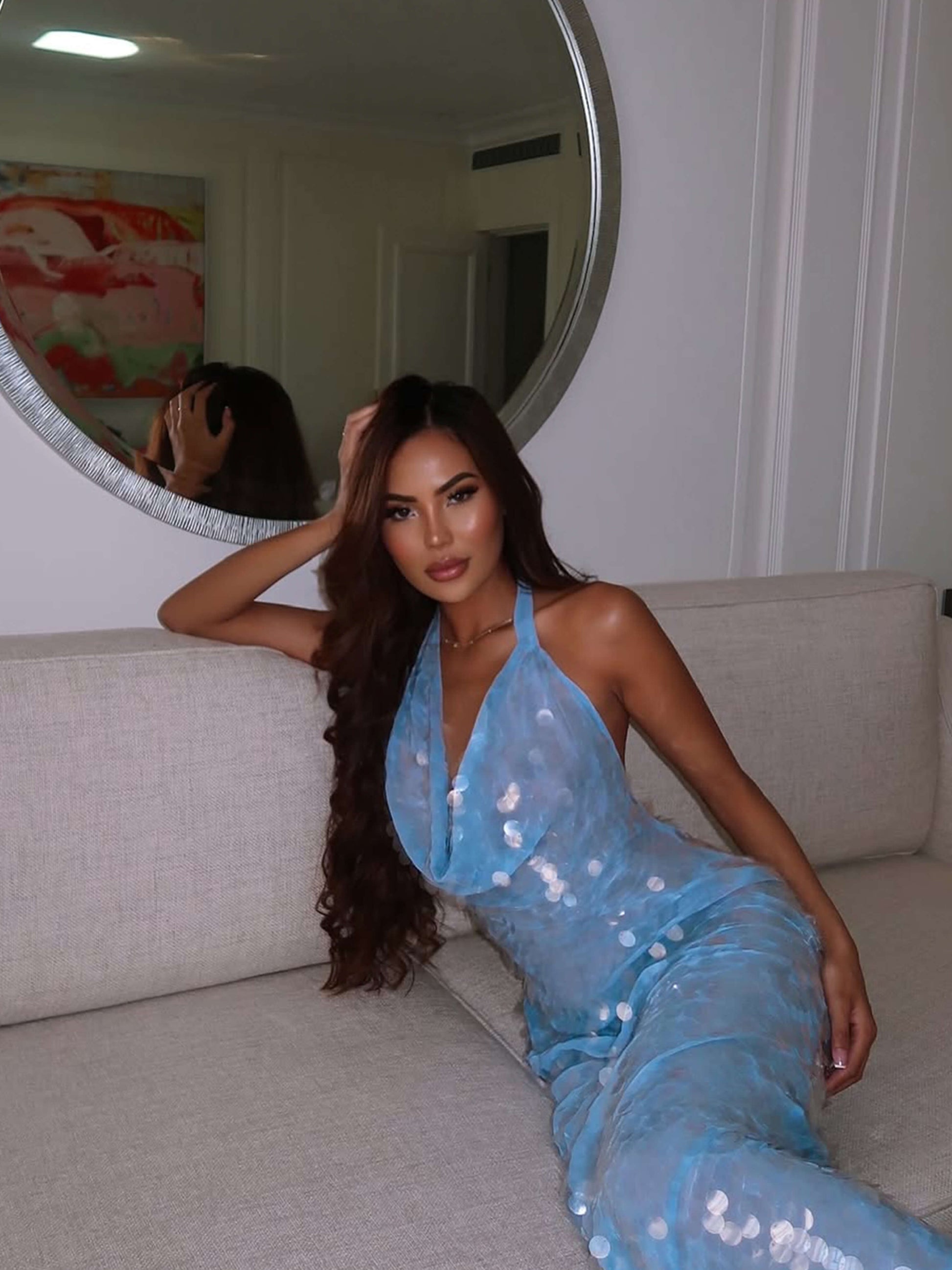 Sequin halter maxi dress in light blue, showing the cowl neckline and full-length skirt while sitting on a couch.