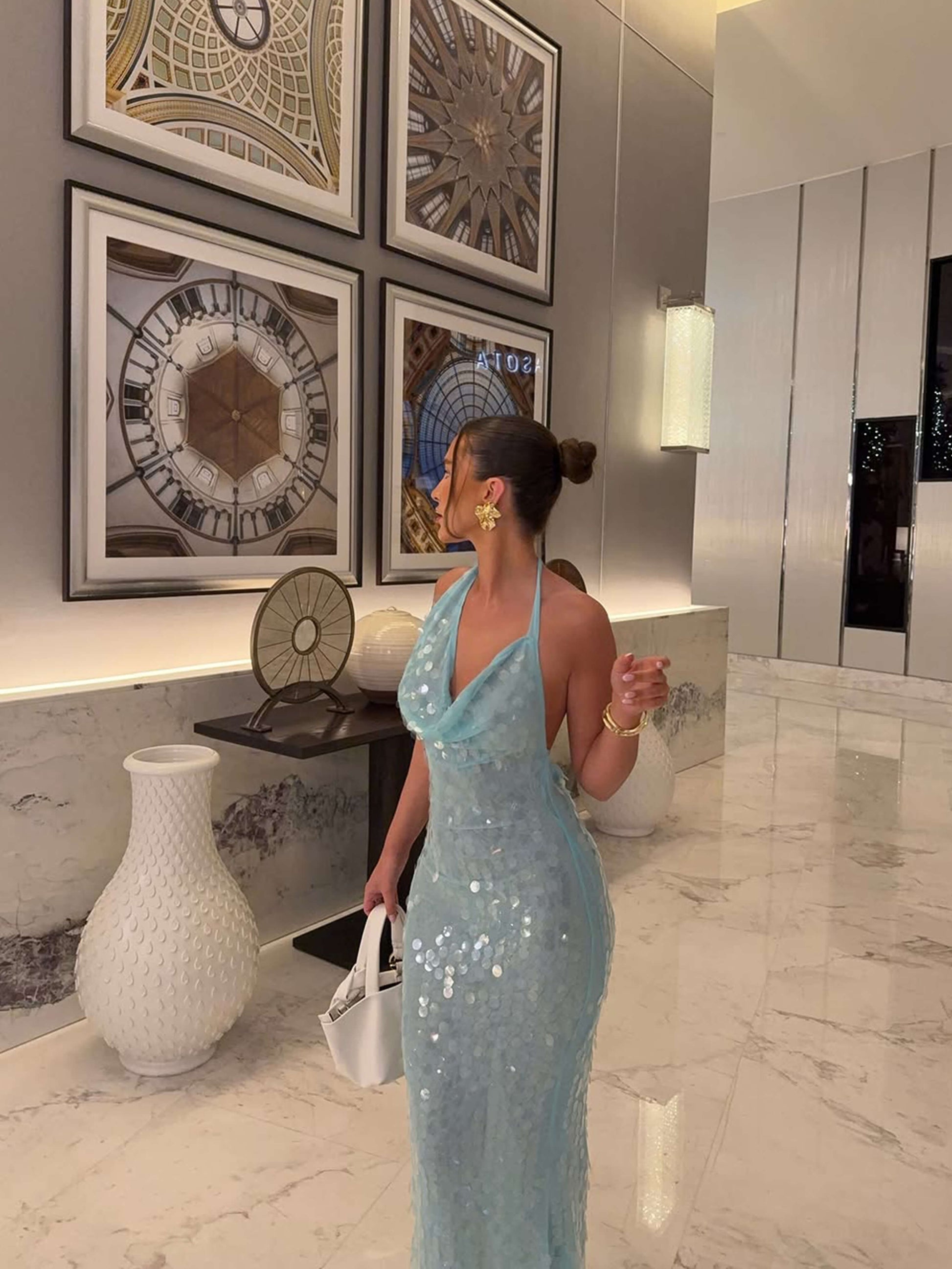 Full view of a light blue sequin halter maxi dress, showcasing the form-fitting design and sparkling details in a hallway.