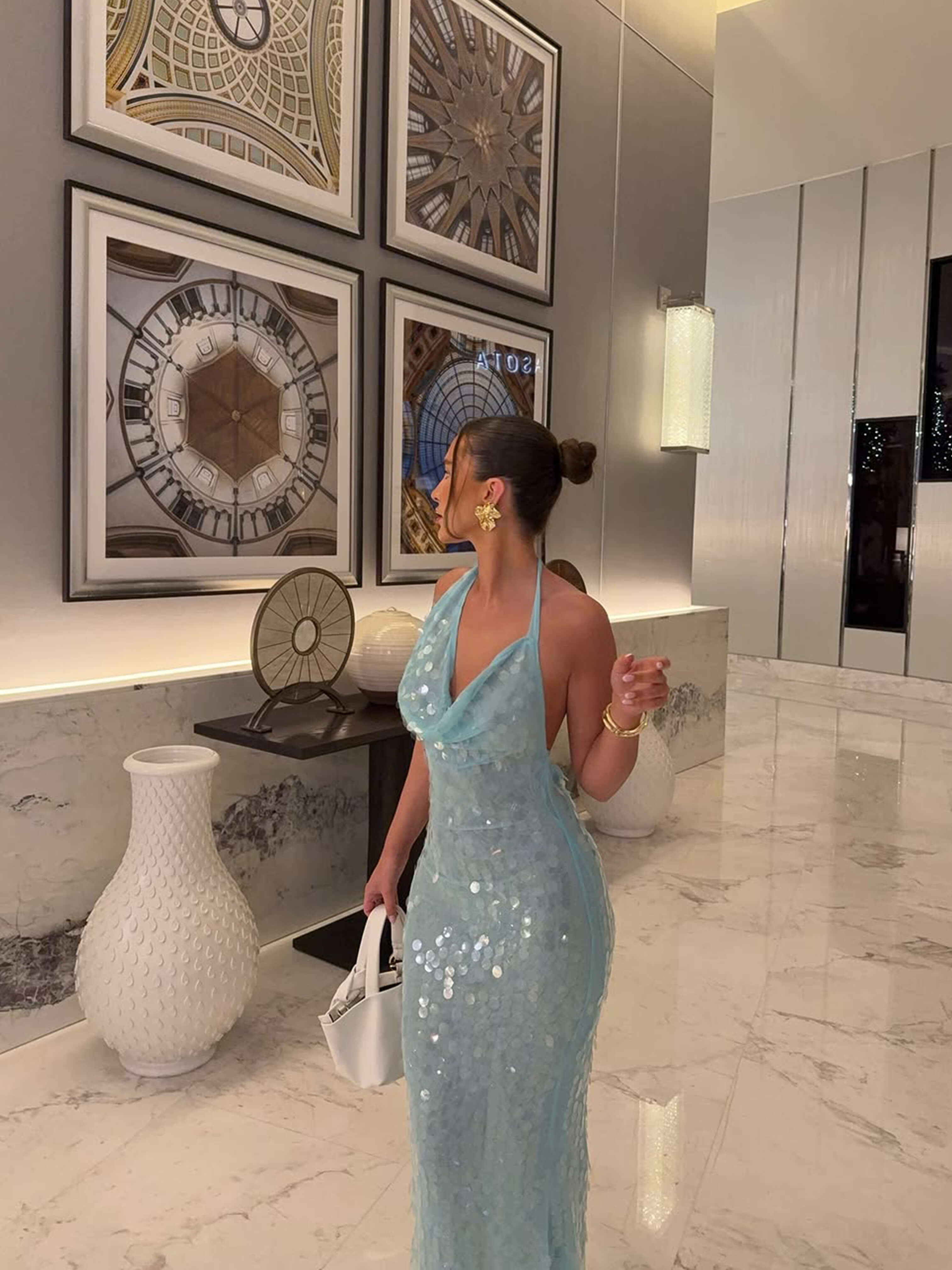 Full view of a light blue sequin halter maxi dress, showcasing the form-fitting design and sparkling details in a hallway.