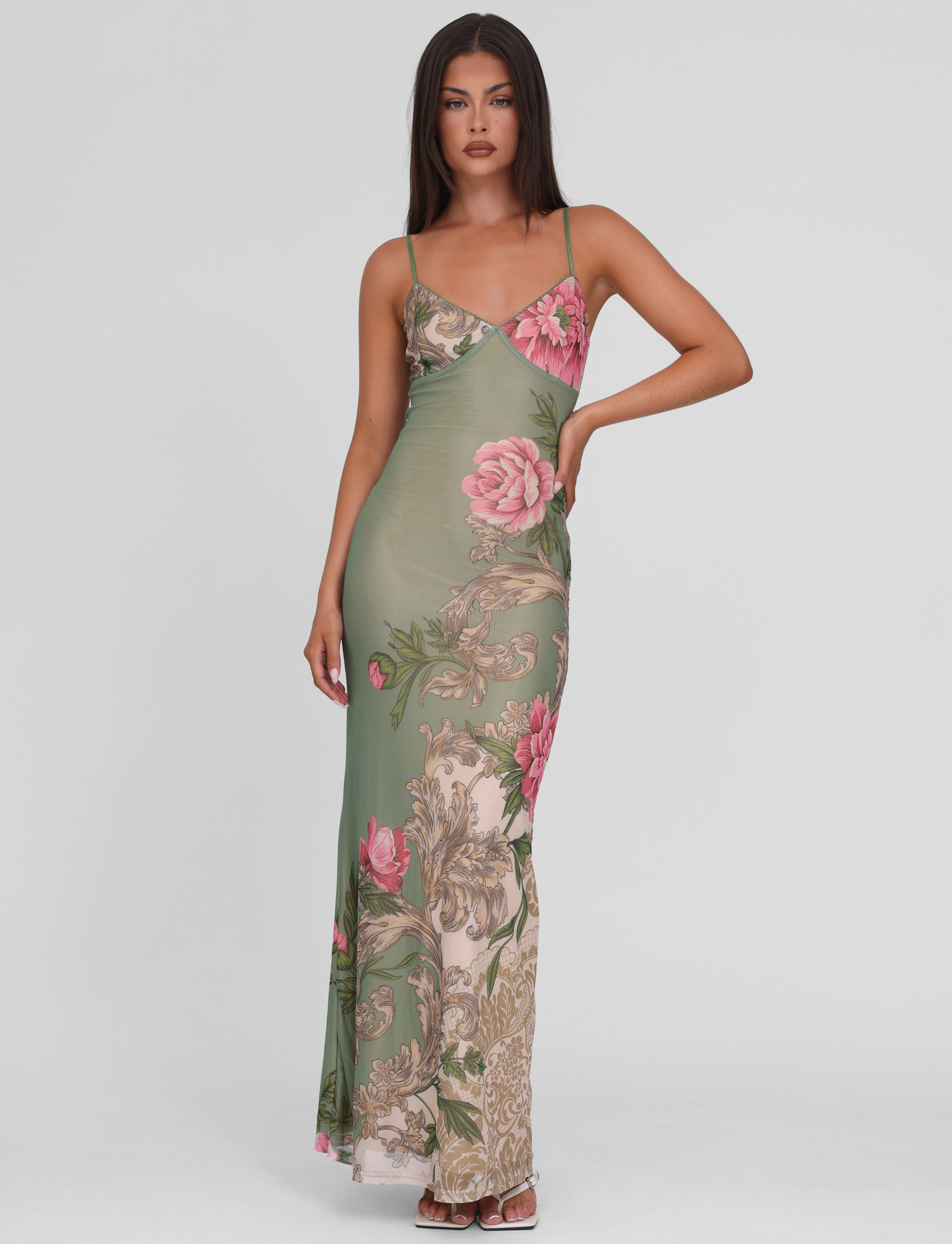 Model posing in Thea Floral Maxi Dress, a sage green slip dress with delicate straps and pink floral details, on a white background.