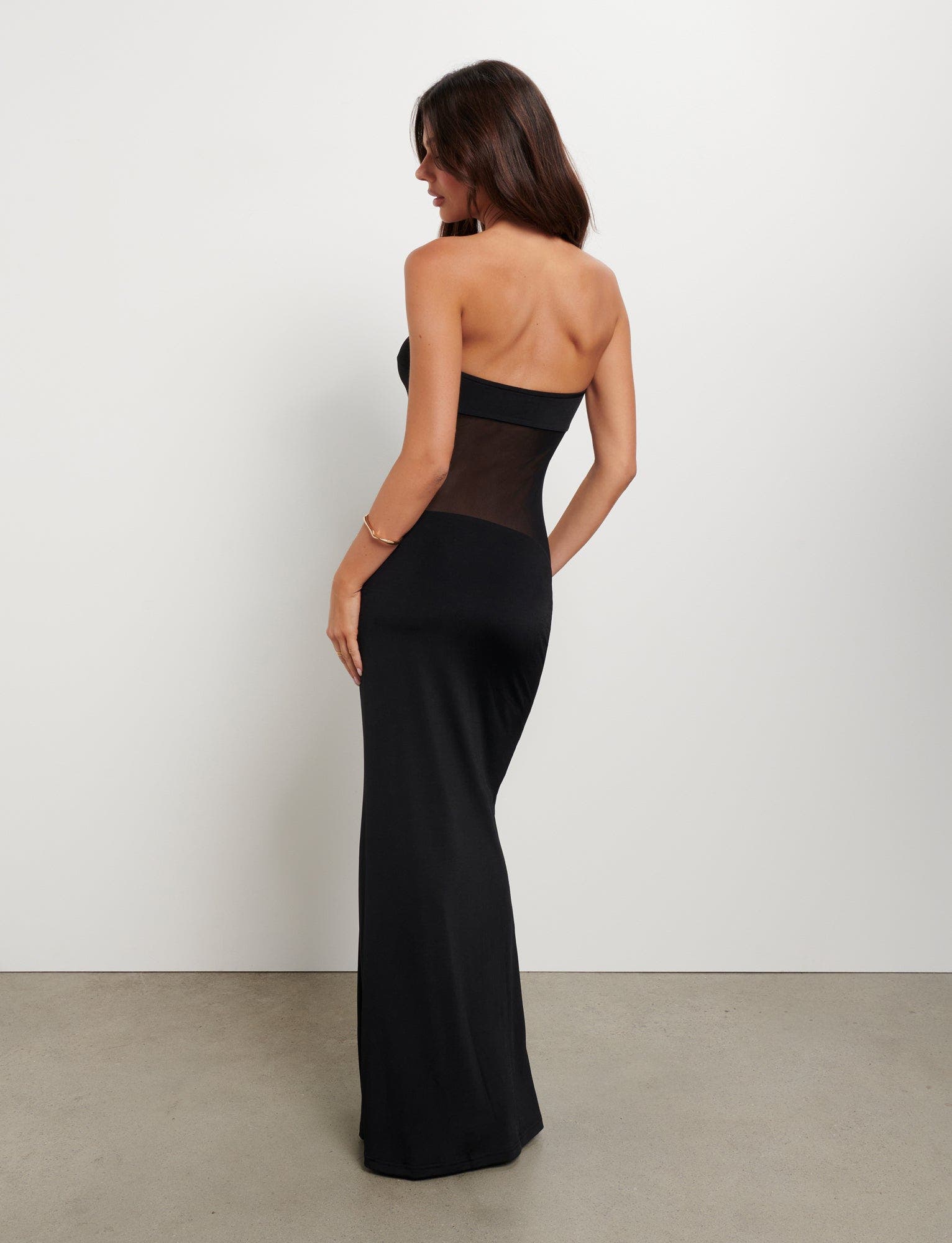 Back three-quarter view of a black strapless Valeria maxi dress with a sheer mesh midriff, showing the elegant drape.