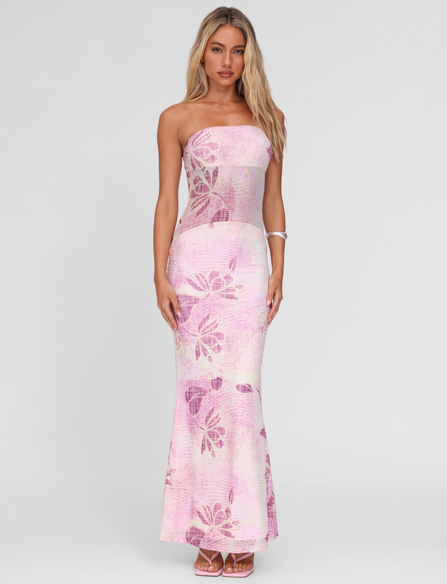 Front view of a blonde model wearing a light pink and purple floral strapless Valeria maxi dress with high heels.