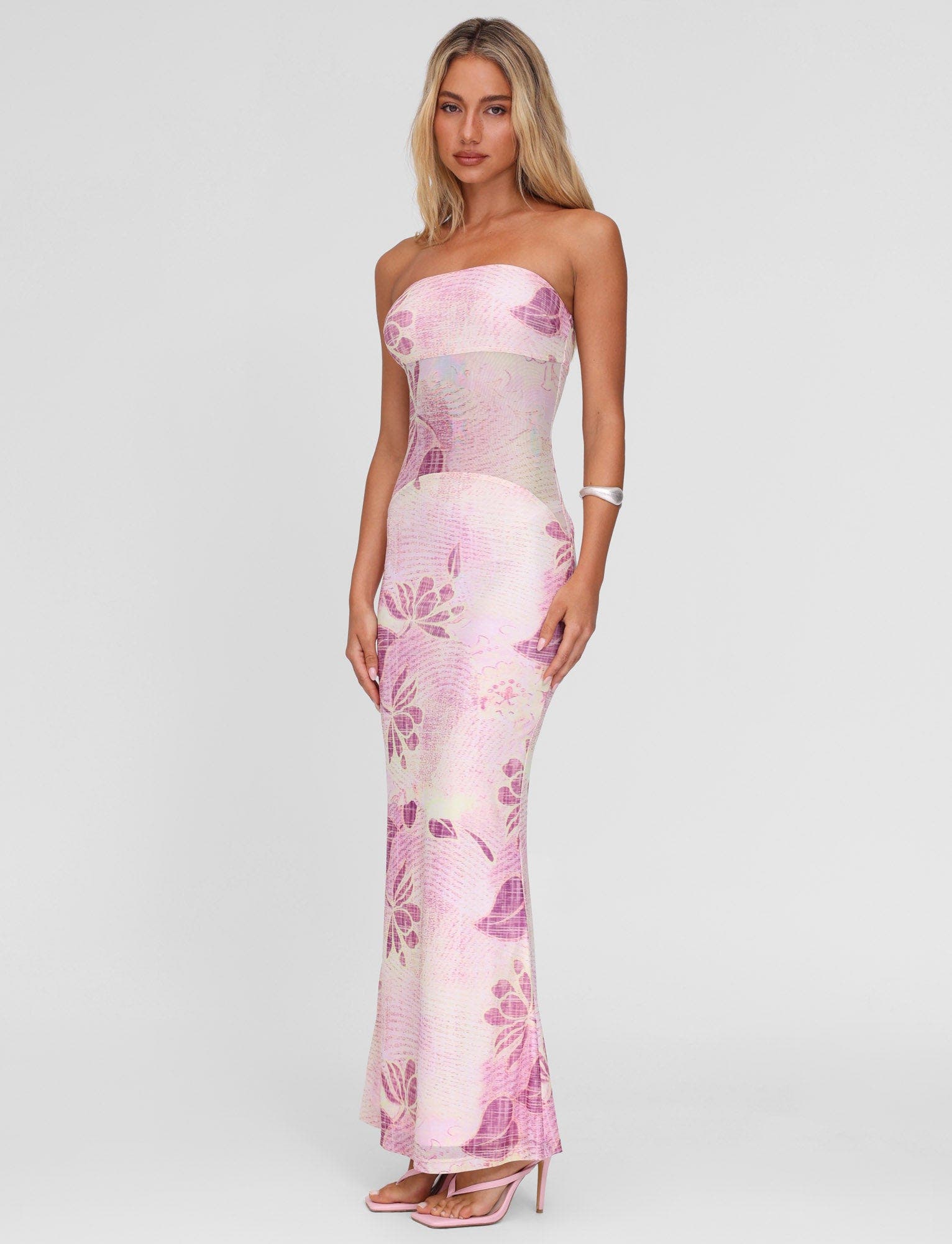 Side profile of a blonde model in a light pink and purple floral strapless Valeria maxi dress, showcasing the full length.