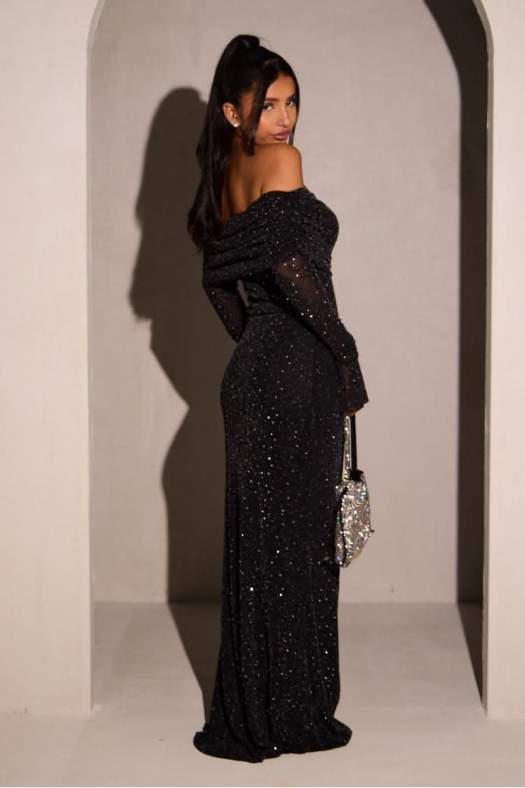 Side view of the black glitter maxi dress, highlighting the fitted silhouette and floor-length skirt, with a sequin handbag.