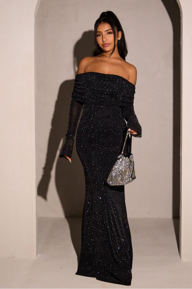 Full-length black glitter maxi dress with off-the-shoulder neckline and long sleeves, paired with a silver sequin handbag.