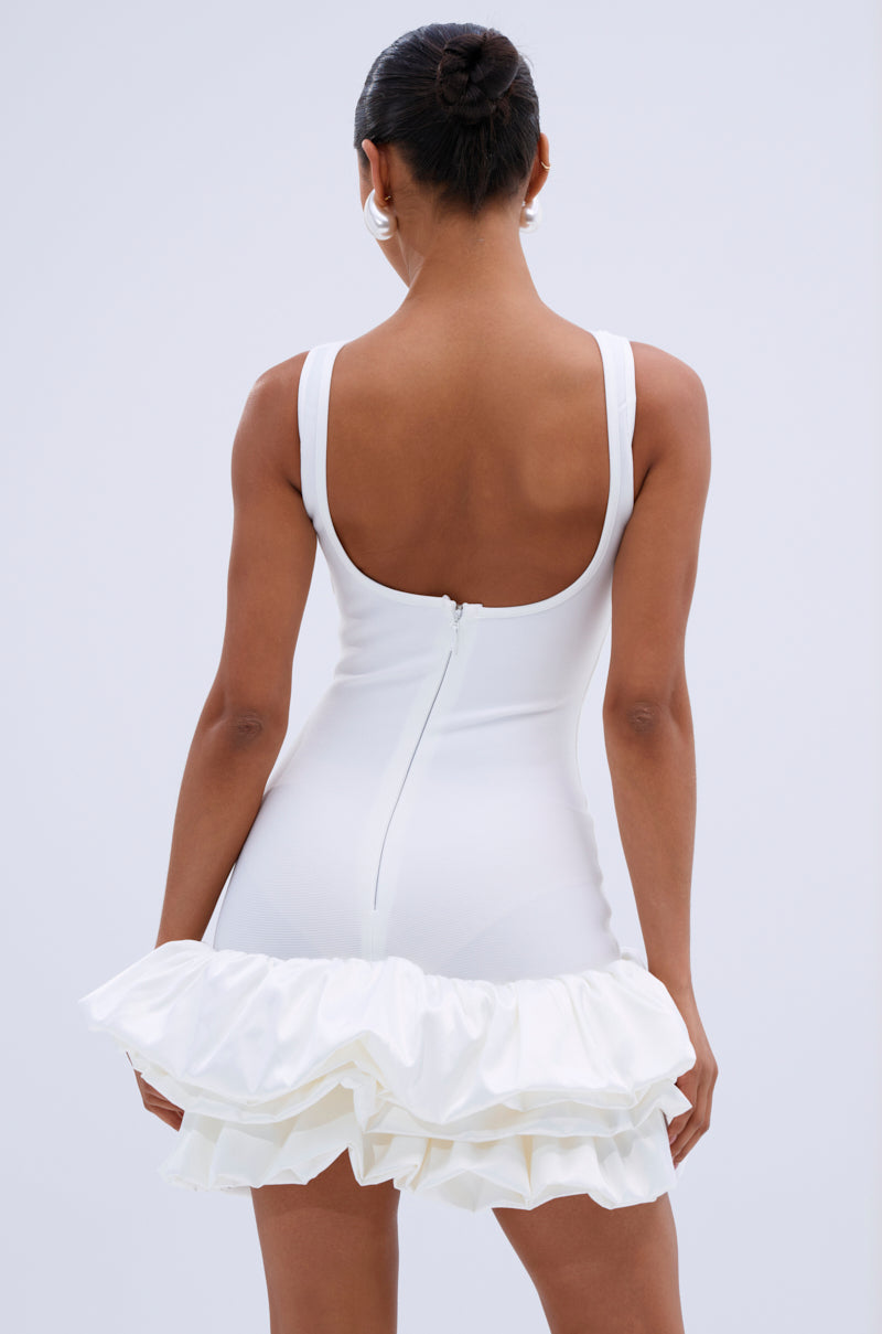 Back view of a model wearing the white Vienna Rosette Mini Dress, revealing a low back and zipper detail.