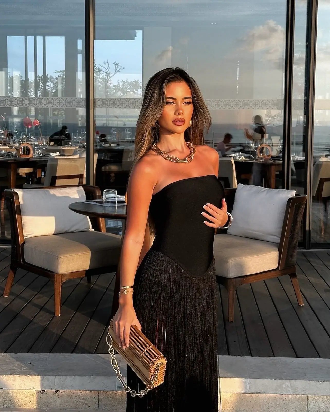 Sleek black strapless maxi dress with a violet fringe skirt, paired with a chunky gold chain necklace and wooden clutch.