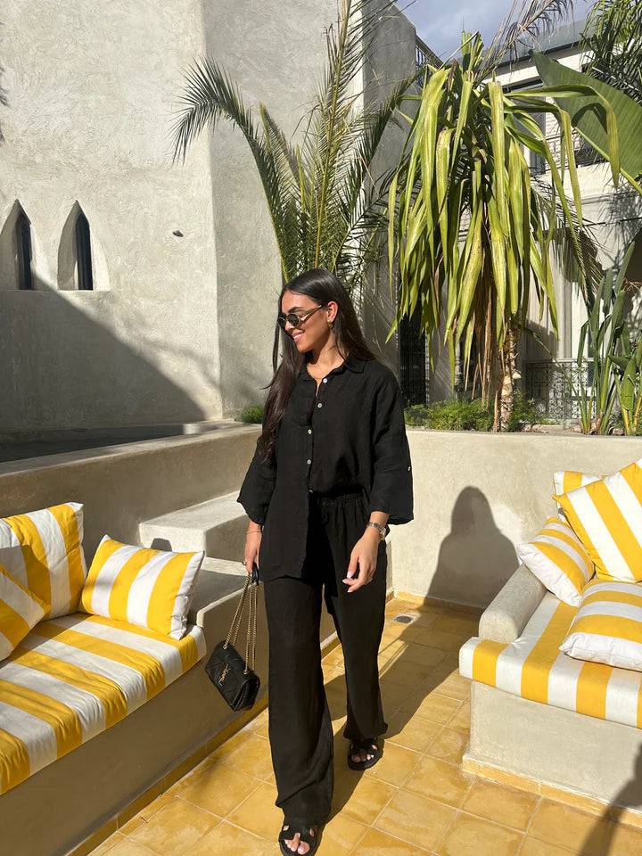 Viviana two-piece linen set in black, with a long-sleeved button-down shirt and matching wide-leg pants, styled with black sandals and a small black purse.