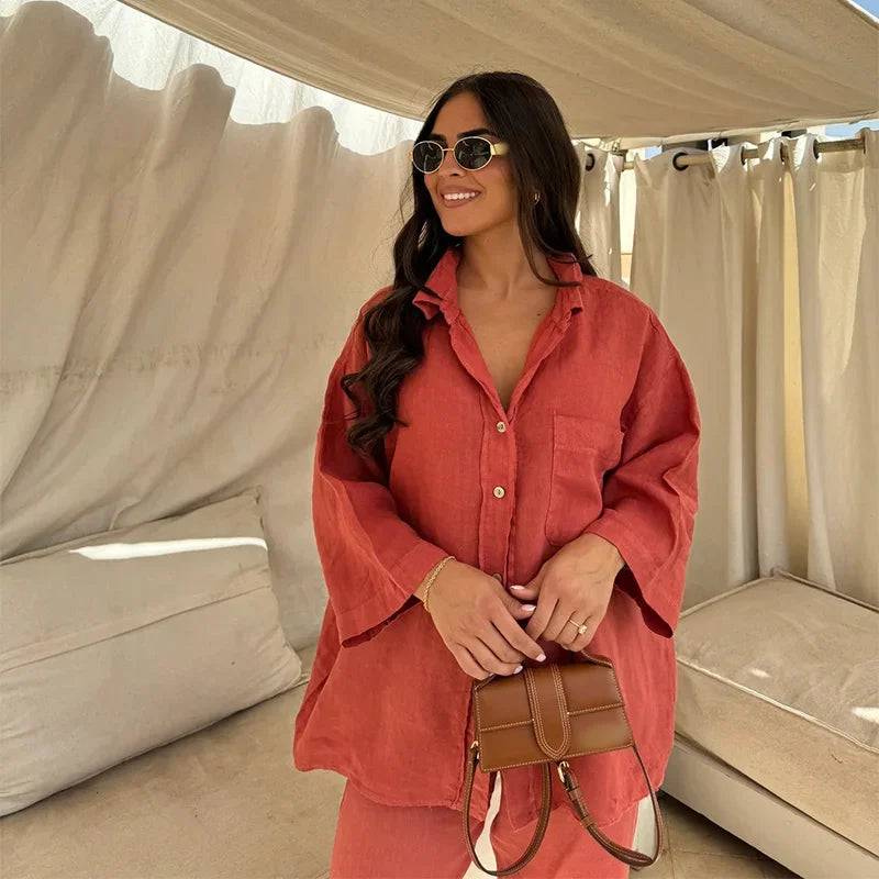 Viviana two-piece linen set in terracotta red, featuring a relaxed-fit button-down shirt and wide-leg pants, accessorized with sunglasses and a small brown handbag.