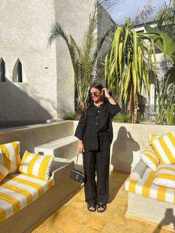 Full body shot of the Viviana two-piece linen set in black, with an oversized shirt and wide-leg pants, worn with black sandals and a small black bag.