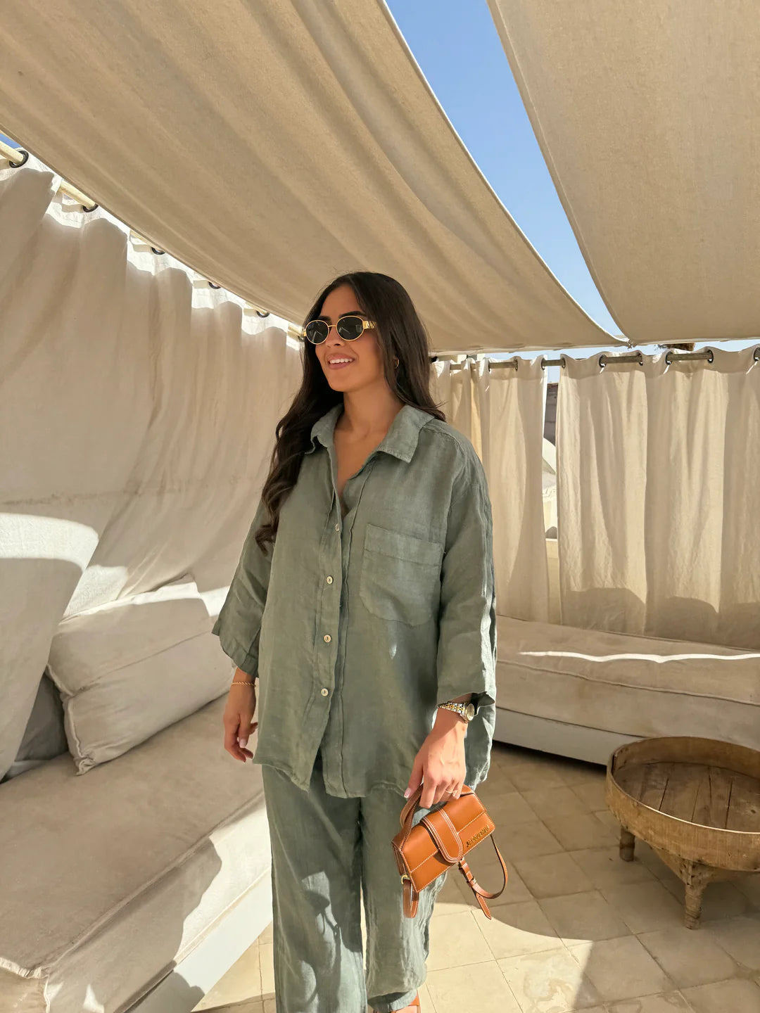Viviana two-piece linen set in sage green, featuring an oversized button-down shirt and relaxed-fit pants, worn with sunglasses and a small brown handbag.