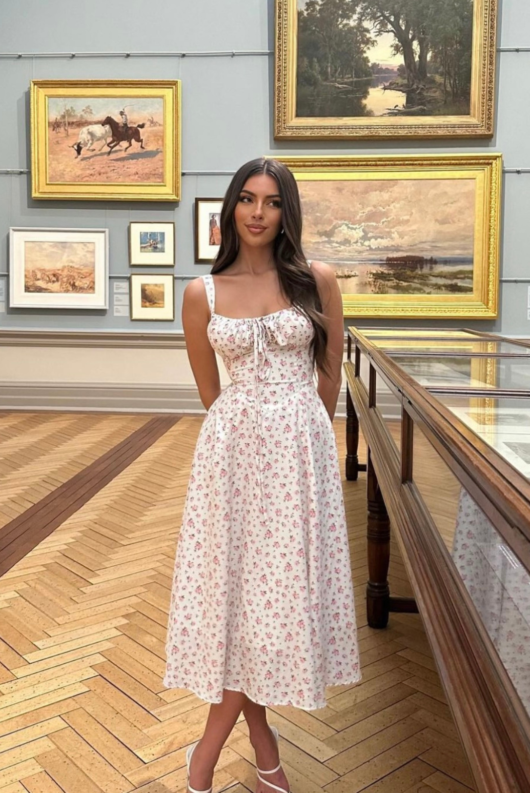 White floral midi dress with pink flower print, ruched bust, and front tie detail, worn outdoors.