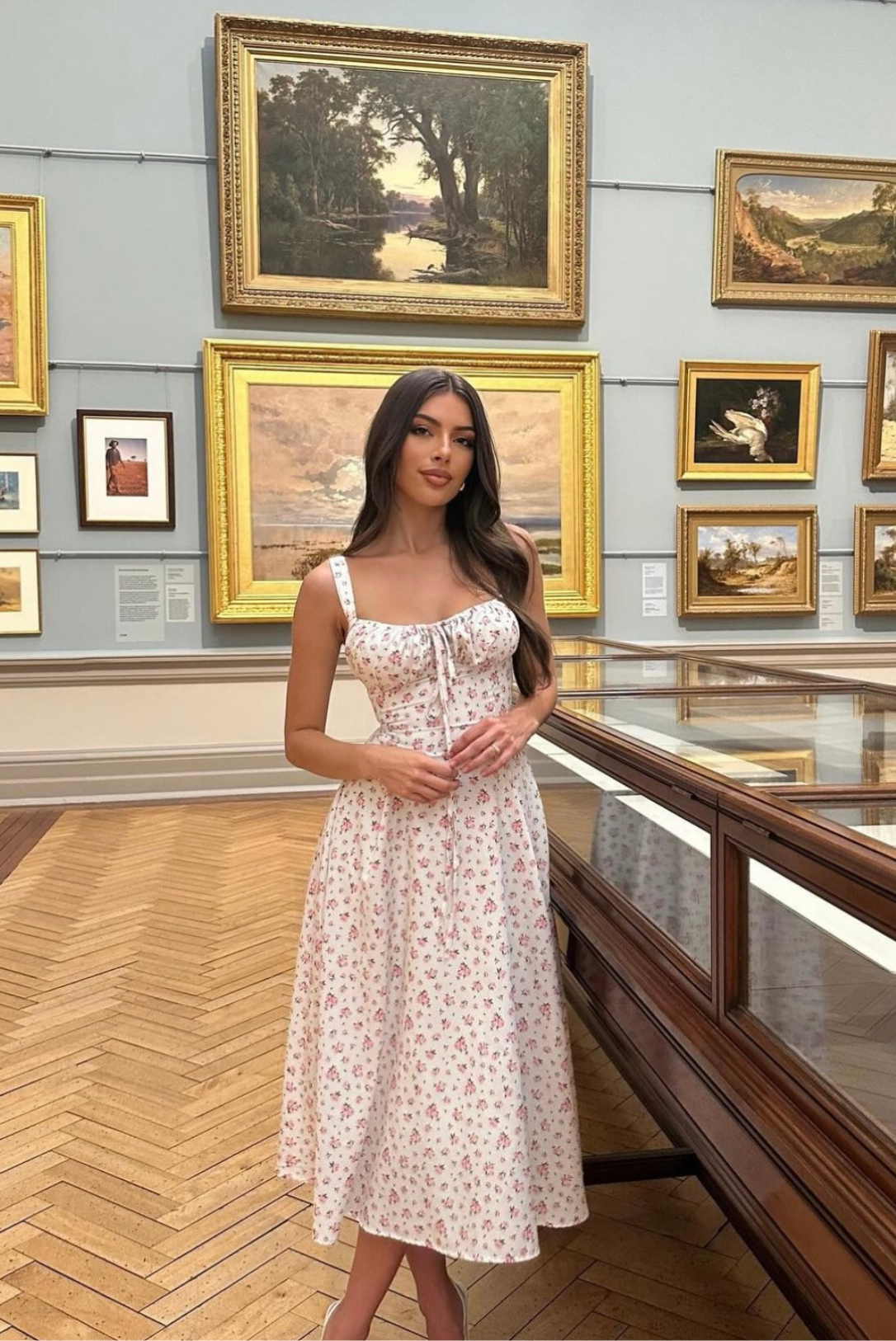 Elegant white floral midi dress with delicate pink flowers and adjustable front ties, in a museum.
