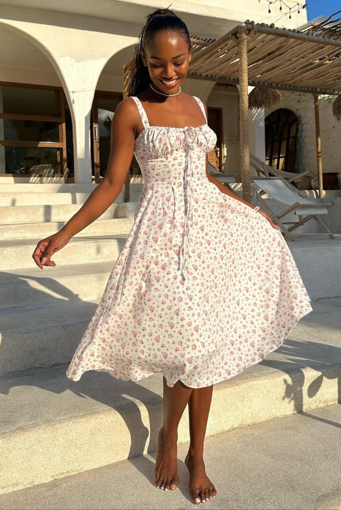 Woman twirling in a white floral midi dress with a sweetheart neckline and pink flower print, outdoors.